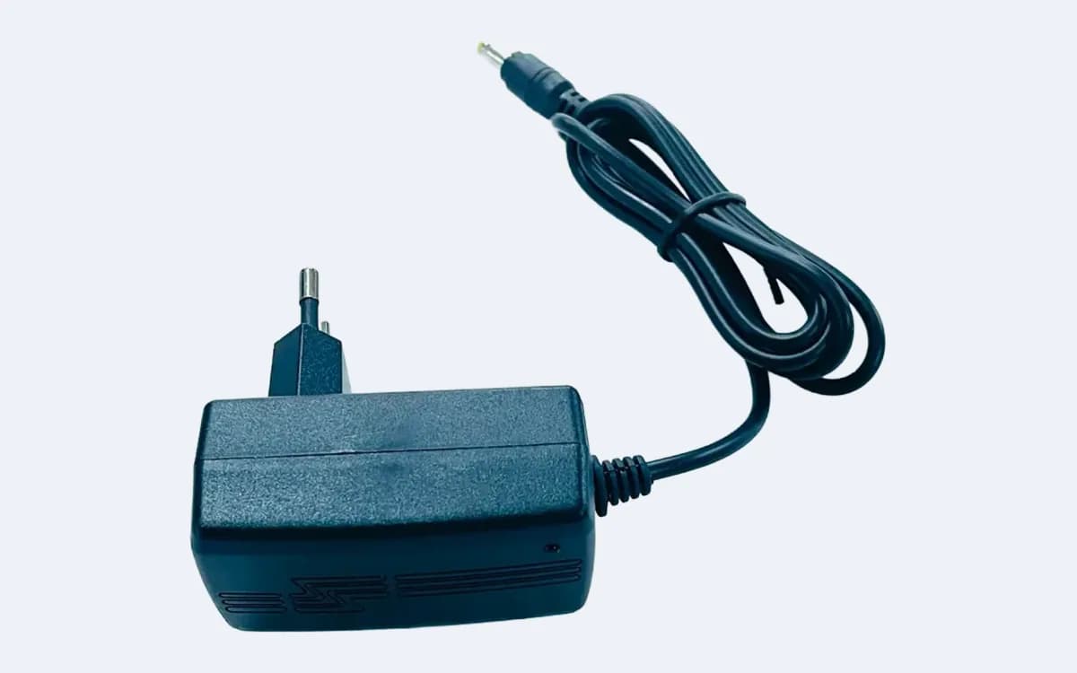 Adaptörün havalandırma kanallı yan yüzü — şebeke fişi solda, sarı uçlu besleme kablosu üstte sarılı