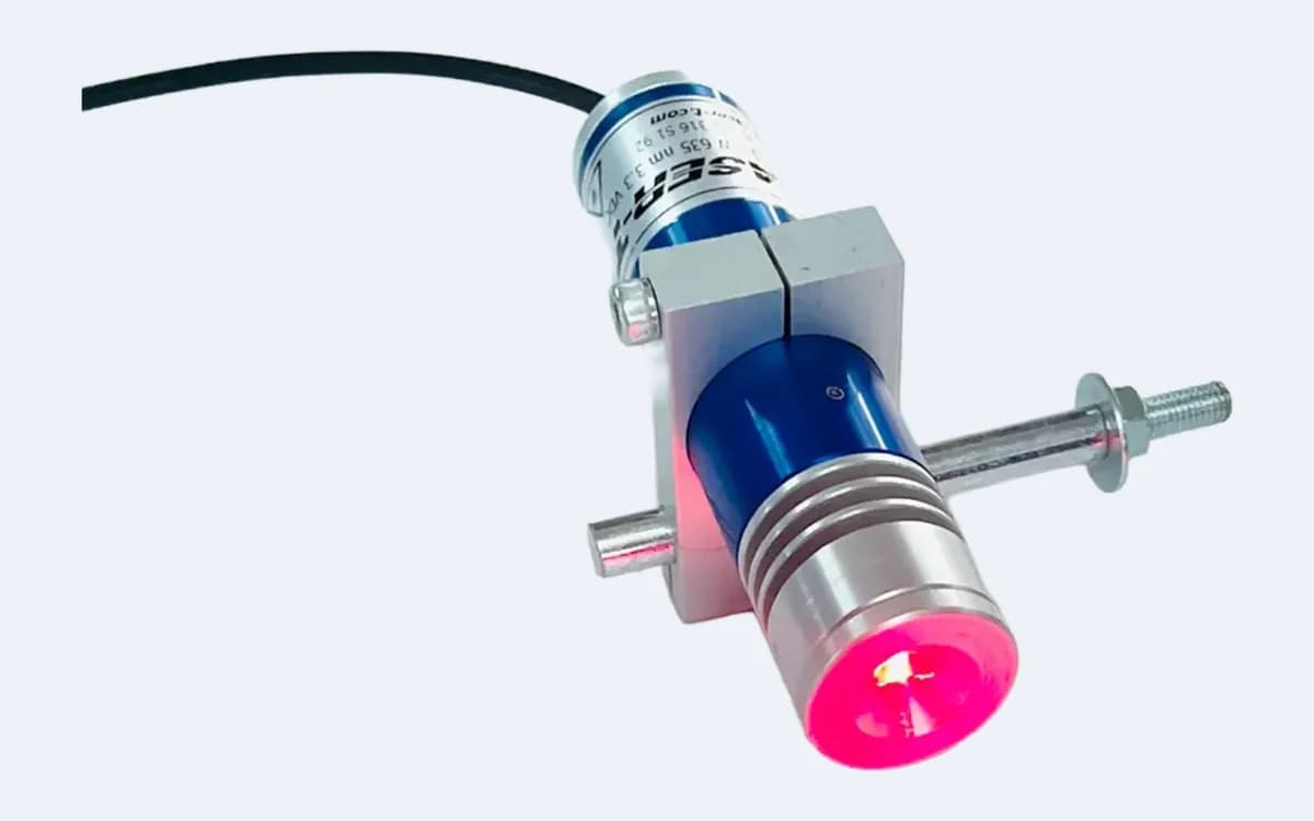 TM200L35 çizgi lazer lens önden, kırmızı yanarken — montaj mili tutucudan sağa uzanıyor, kablo sol üstte