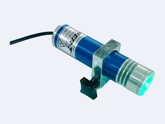 TM100L35 yeşil çizgi lazer çapraz açıdan — lens sağ altta yeşil yanıyor, sıkma topuzu tutucunun altında, kablo solda